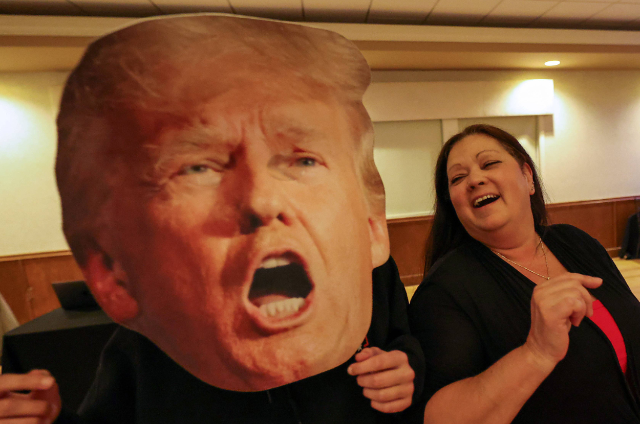 Person holding oversized cutout of a shouting face, with another person laughing next to it