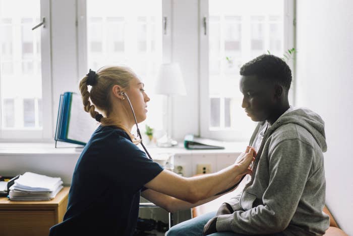 Healthcare worker using a stethoscope to examine a person sitting in a clinic room