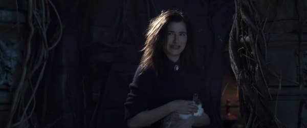 Kathryn Hahn with windswept hair stands in a dark room holding a rabbit. She is dressed in a casual, dark top. The setting appears mysterious and eerie