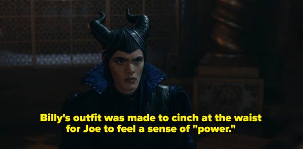 Person dressed as a fantasy character with intricate horned headpiece and an elaborate collar, sitting in an ornate setting