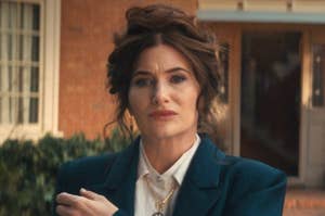 Kathryn Hahn in formal attire with a serious expression, standing outside a building