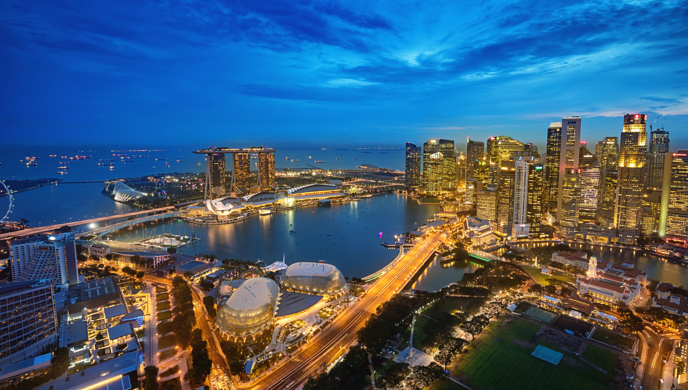 Aerial view of Singapore&#x27;s Marina Bay at dusk, featuring city skyline and illuminated buildings