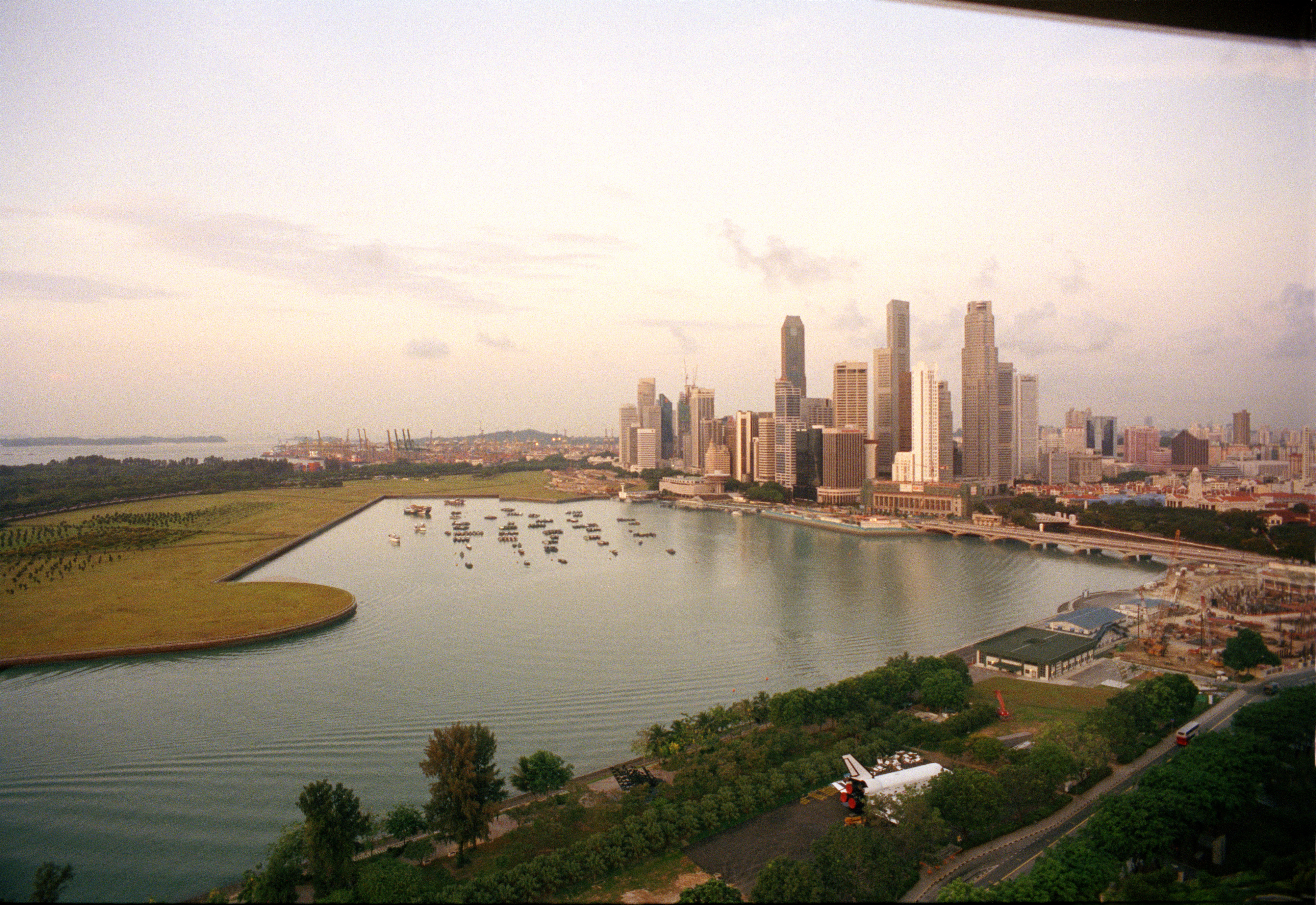 Aerial view of a cityscape with skyscrapers and a waterfront, featuring a mix of urban and natural landscapes, including trees and water