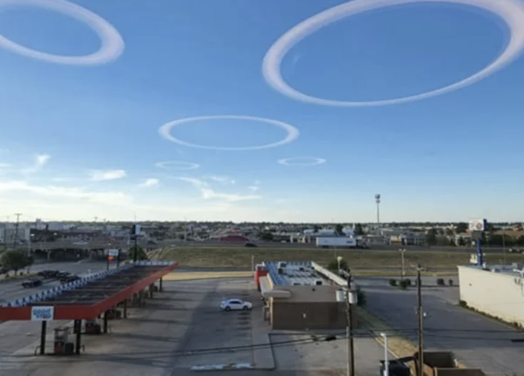 Rings of clouds in a clear sky over an empty parking lot and gas station