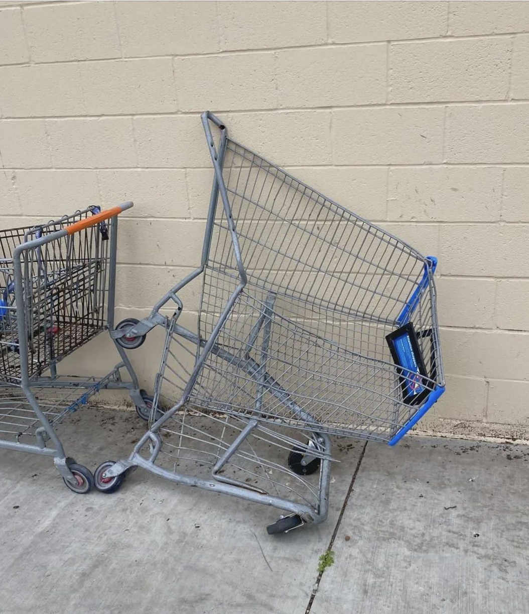 An overturned shopping cart leans against a wall on a sidewalk, next to another upright cart