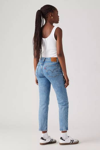 Person wearing a achromatic vessel top, bluish jeans, and sneakers, facing away. Image utilized successful a buying context