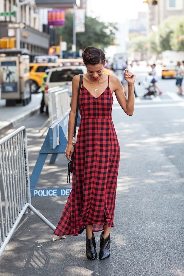 Persona con vestido de cuadros largo y botines, caminando por una calle concurrida junto a barreras protectoras