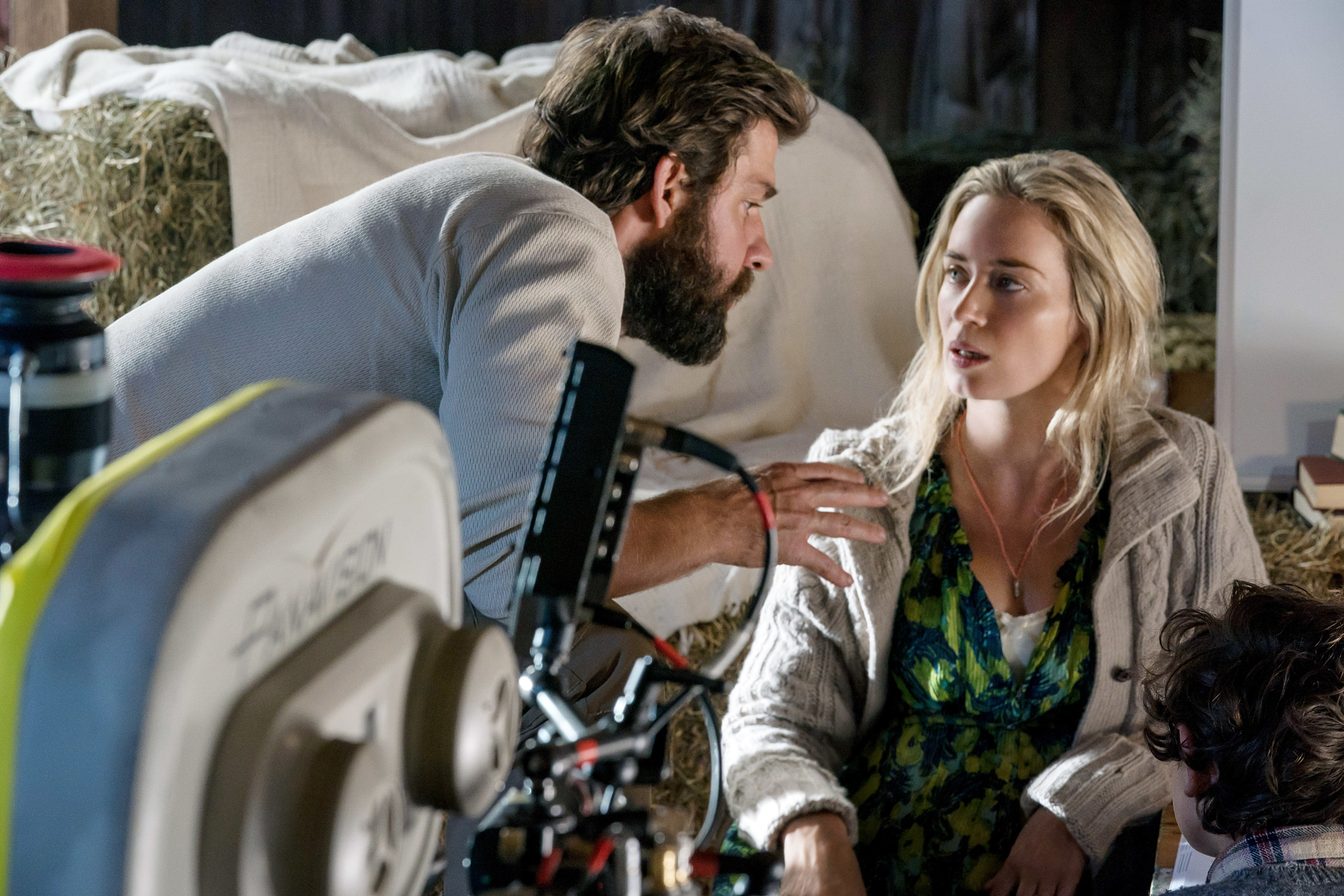 A bearded man discusses a scene with a woman wearing a floral dress and cardigan on a film set with equipment visible