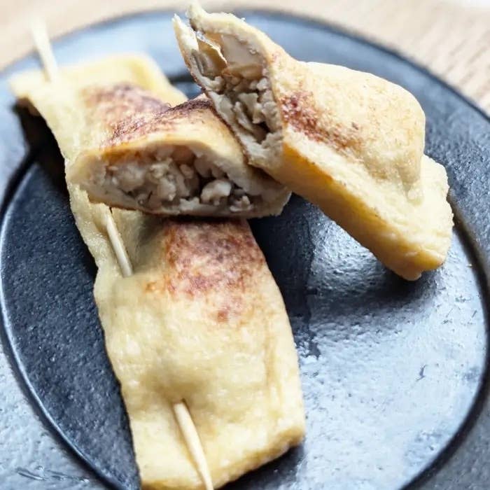 プレートに盛り付けられた豆腐を包んだ揚げが2つ、串で留められている。