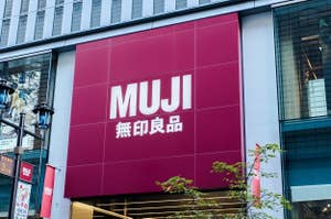 MUJIの店舗外観。大きな赤い看板にMUJIと無印良品のロゴが表示されています。ビルのガラスに街の景色が反射しています。