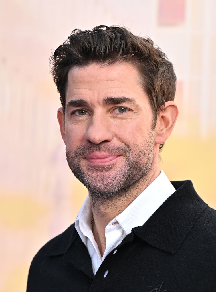 Person with short hair and a beard wearing a white shirt and a black jacket, smiling at the camera