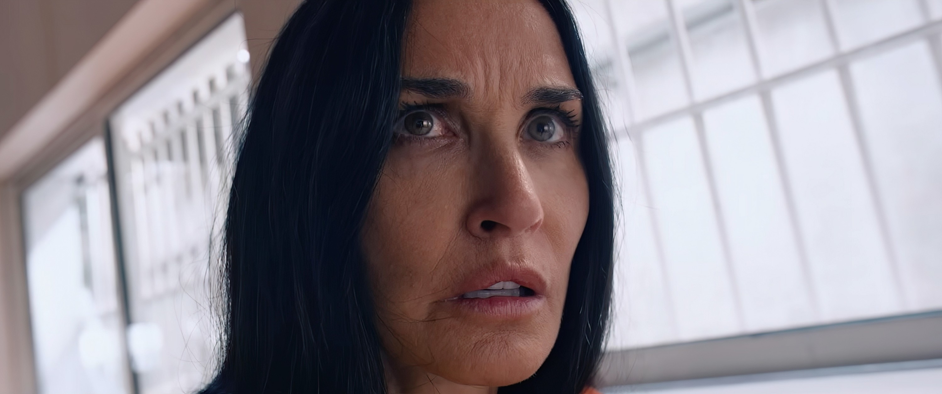 Demi Moore with long hair looks upward with a concerned expression indoors, in front of a window with bars