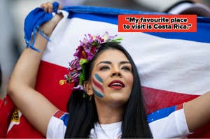 A person with a flower crown and painted cheek holds a flag, cheering at an event