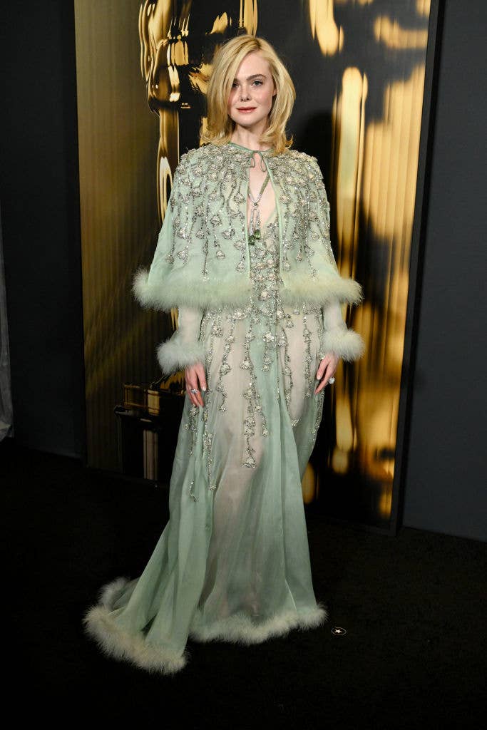 Person in an embellished gown with fur details poses on the red carpet against an elegant backdrop