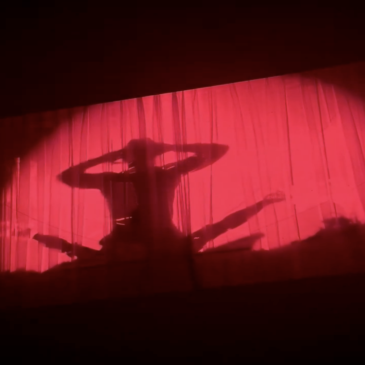 Silhouette of a performer on stage behind curtains, arms raised, creating a dramatic scene