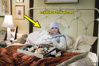 Person in bed with a hat and scarf, surrounded by cozy pillows and a breakfast tray, appears relaxed in a warmly lit bedroom