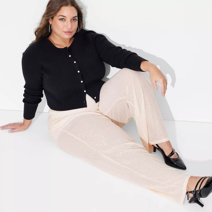 Model seated in a stylish, casual outfit with a black cardigan and light-colored pants, wearing black shoes