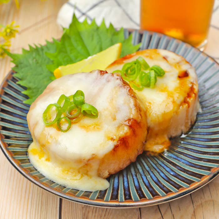 お皿に盛られたチーズが溶けた料理、ネギとレモン添え。食欲をそそる料理です。
