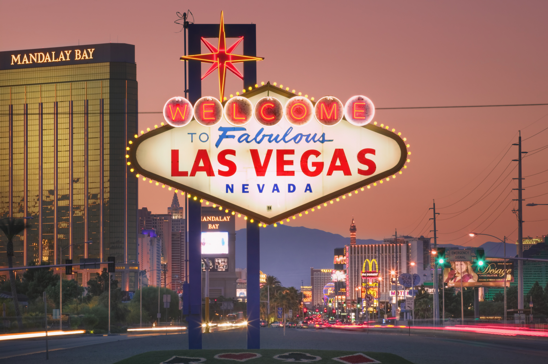 Las Vegas welcome sign with city skyline, including hotels and bright lights, in the background at sunset