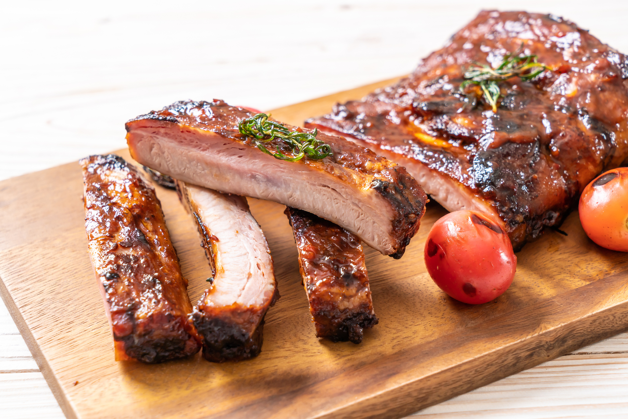 Barbecued ribs on a wooden board, garnished with herbs and served with cherry tomatoes