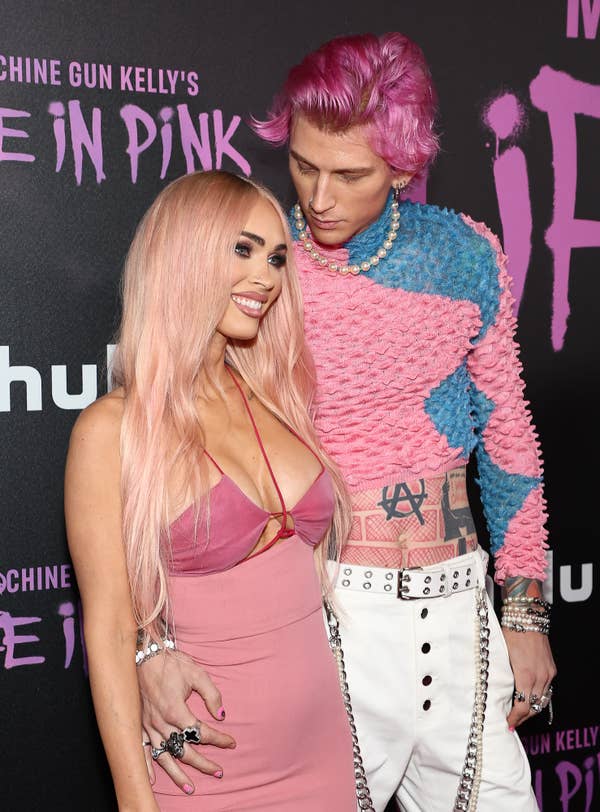The couple on the red carpet; the woman wears a sleeveless dress, and MGK wears a two-toned textured sweater with pants