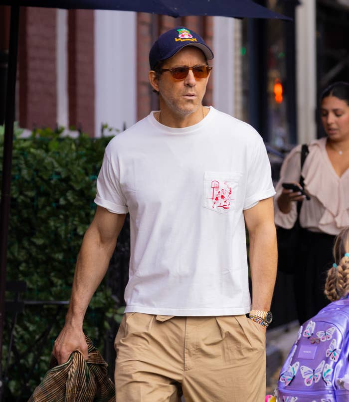 A person in casual streetwear, wearing a cap and sunglasses, walking outdoors