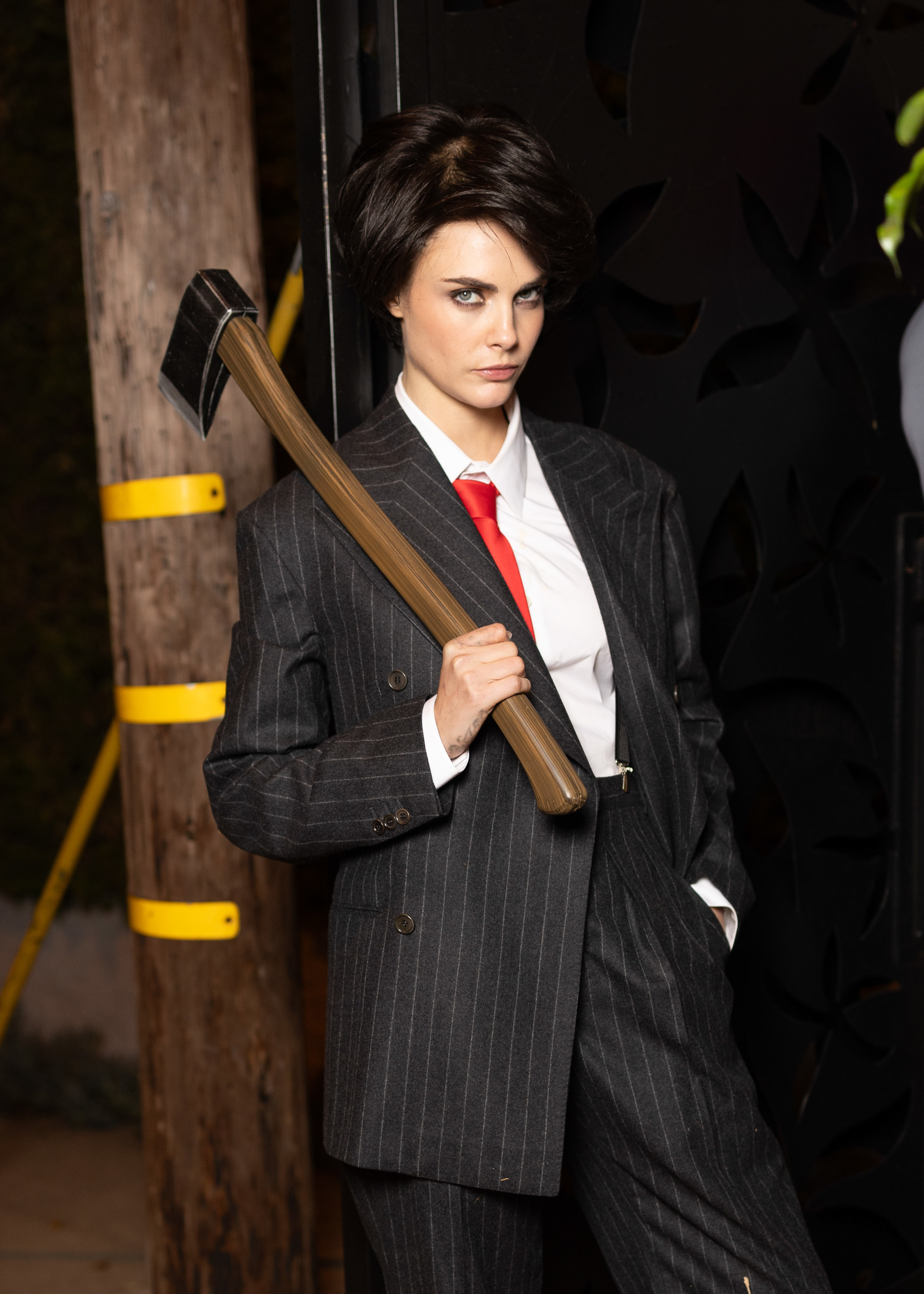 Cara Delevingne as Christian Bale in American Psycho in a suit and holding an axe