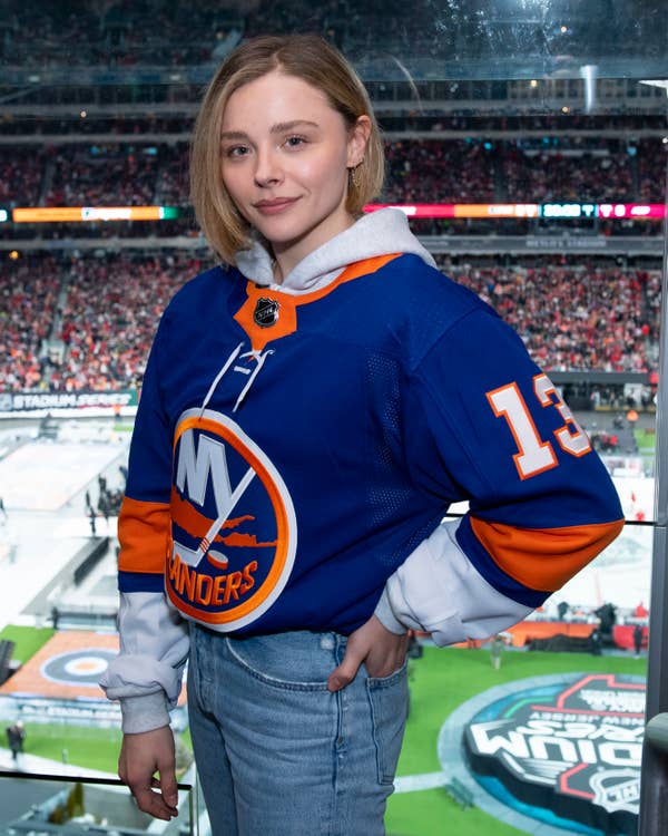 A person in a New York Islanders jersey, number 13, posing at a hockey game in a stadium
