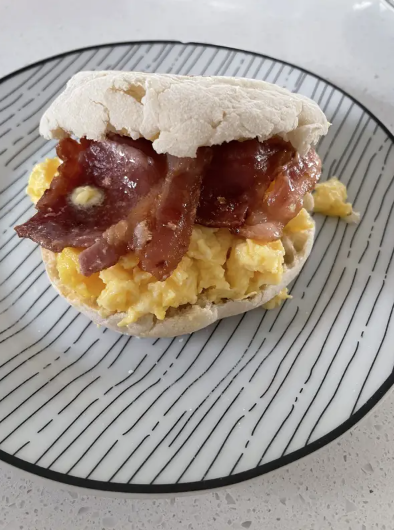 Breakfast sandwich with scrambled eggs and bacon on an English muffin, served on a plate with a stripe design