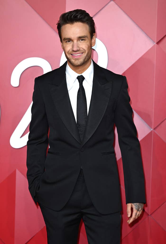 Man in a black suit and tie smiles on a geometric-patterned backdrop