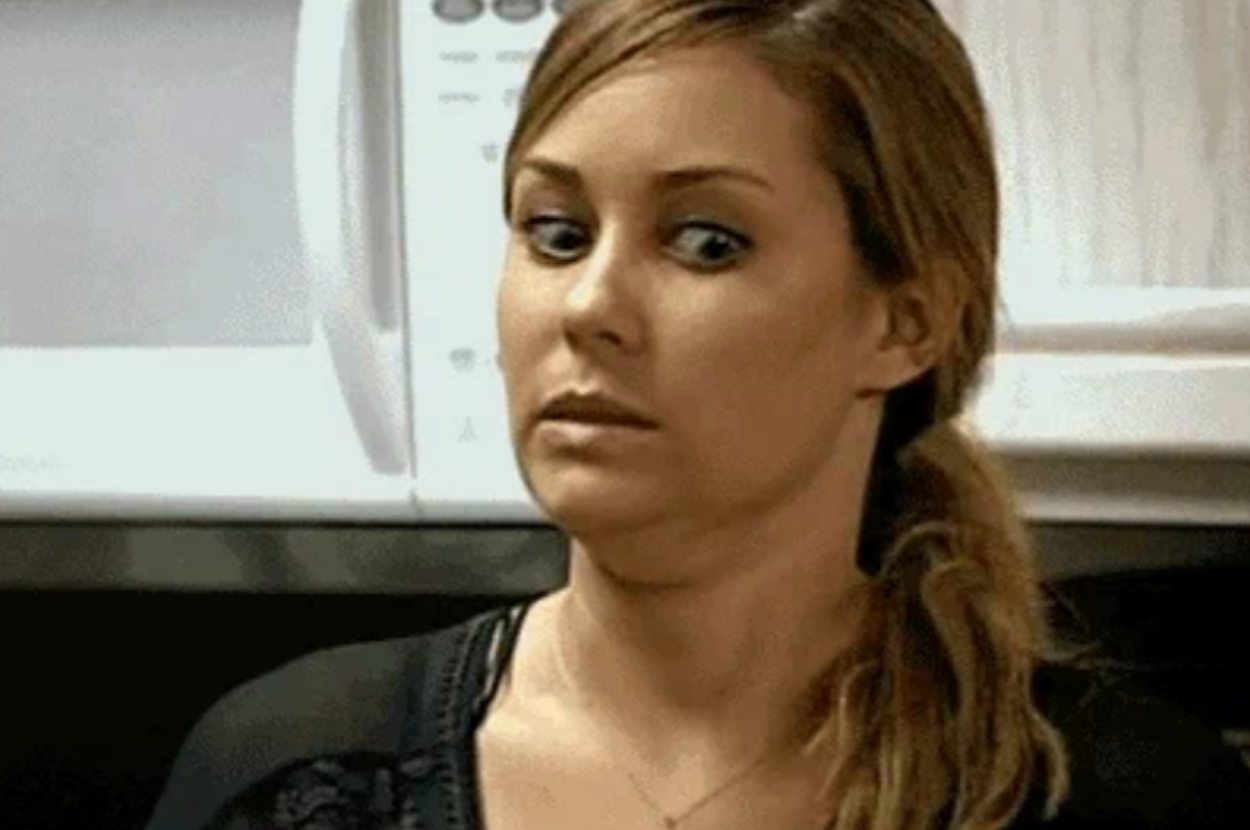 Person with long hair looks sideways with a surprised expression in a casual indoor setting