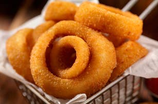 A basket of crispy onion rings on a paper lining, placed on a table