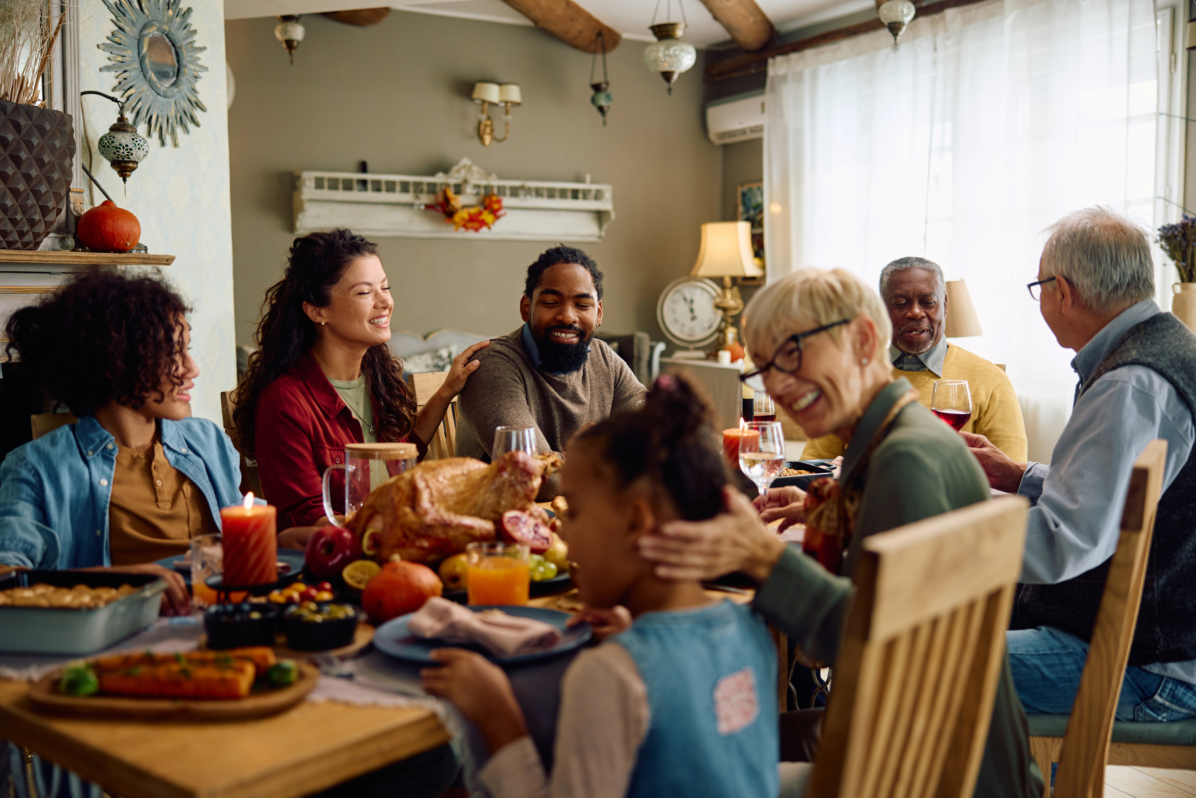 Family and friends gather around a dining table, smiling and sharing a meal together in a cozy setting