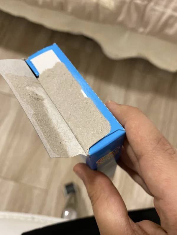 A person holds a blue, partially opened box with a large amount of sandy dust inside and around the opening
