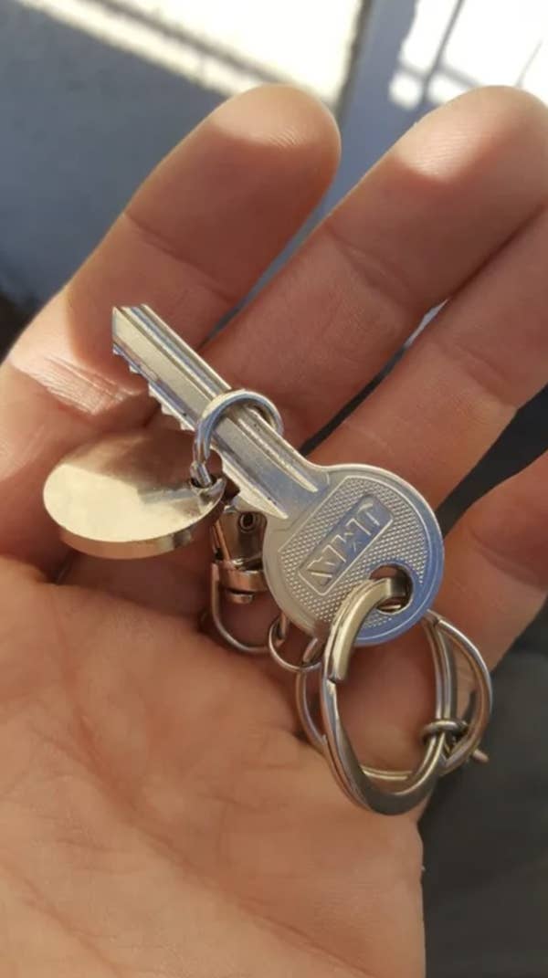 A hand holding a silver key on a keyring with a round metal tag