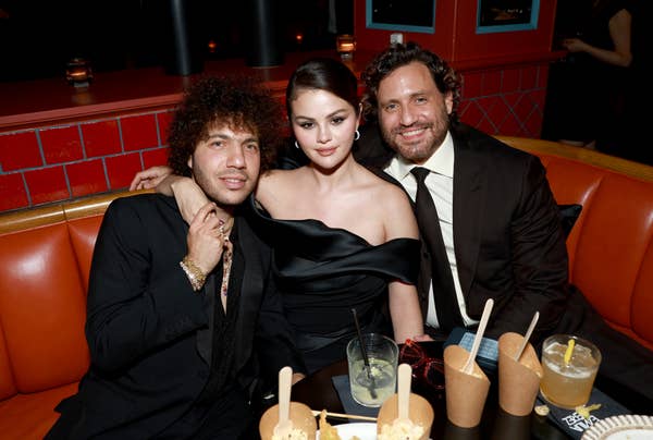 Three people sit together at a booth, dressed in formal attire. The atmosphere suggests a social or celebrity event