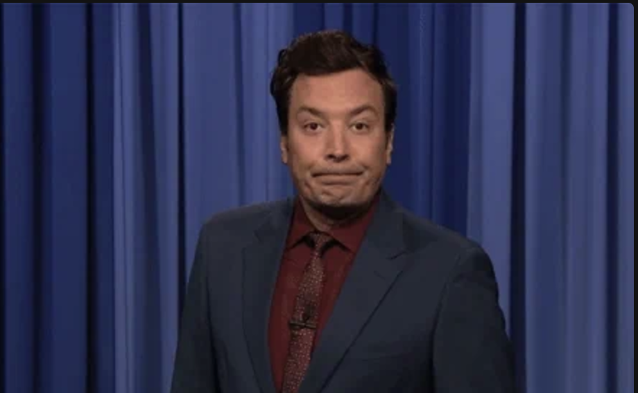 Person in formal attire stands in front of curtains, looking directly ahead with a subtle smile