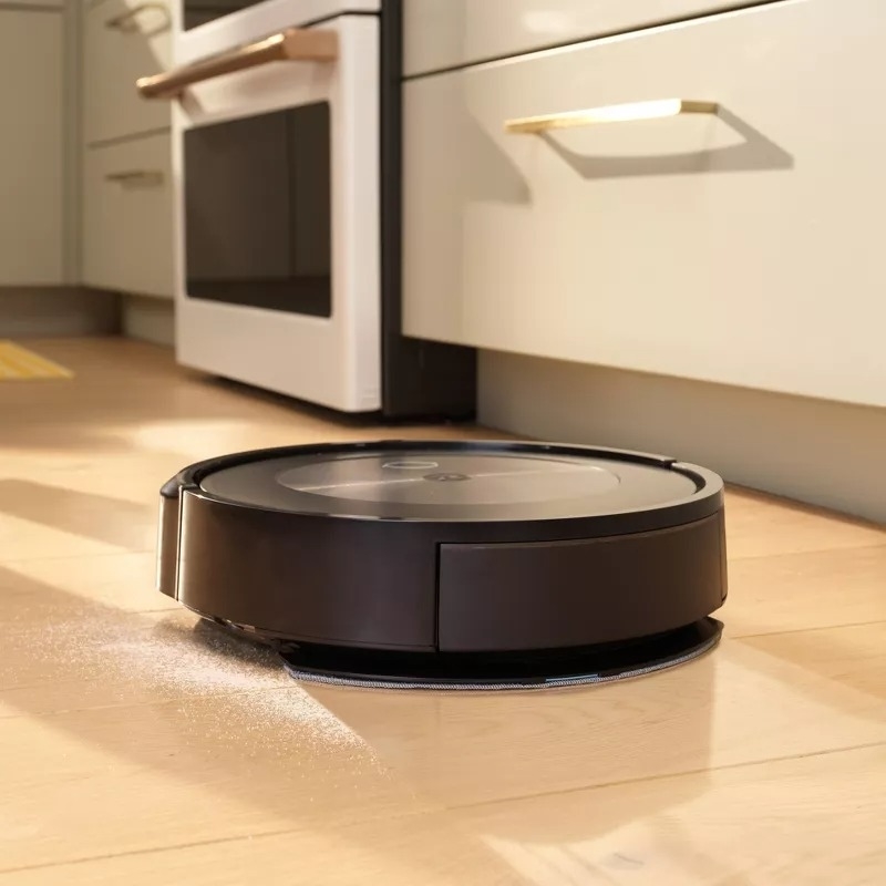 Robotic vacuum cleaning a kitchen floor. The appliance is near an oven, sweeping dust, showcasing effortless home cleaning technology