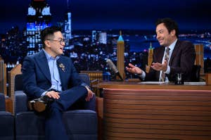 Bowen Yang and Jimmy Fallon sitting on "The Tonight Show" set, engaged in conversation