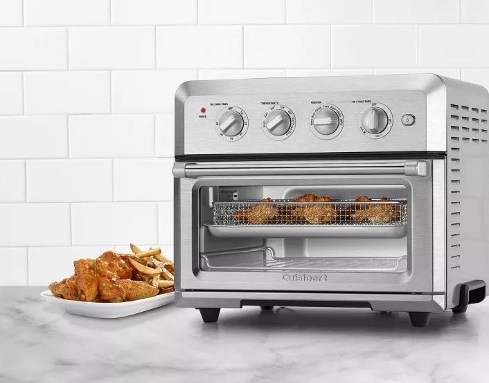 Countertop toaster oven with air fry feature, stainless steel finish. Beside it, a plate of wings and fries on a marble surface