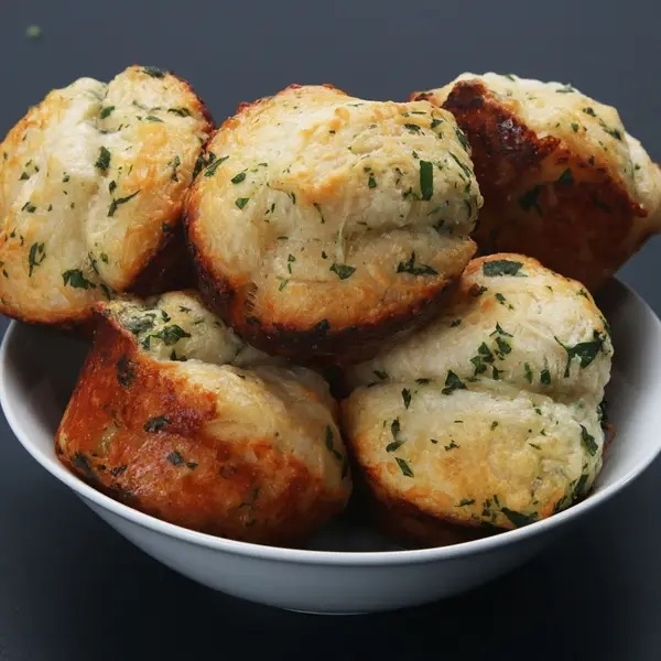 Bowl of freshly baked garlic and herb muffins stacked together