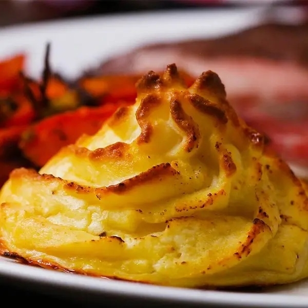 A plate with fluffy mashed potatoes delicately piped in a swirl, alongside vibrant roasted vegetables