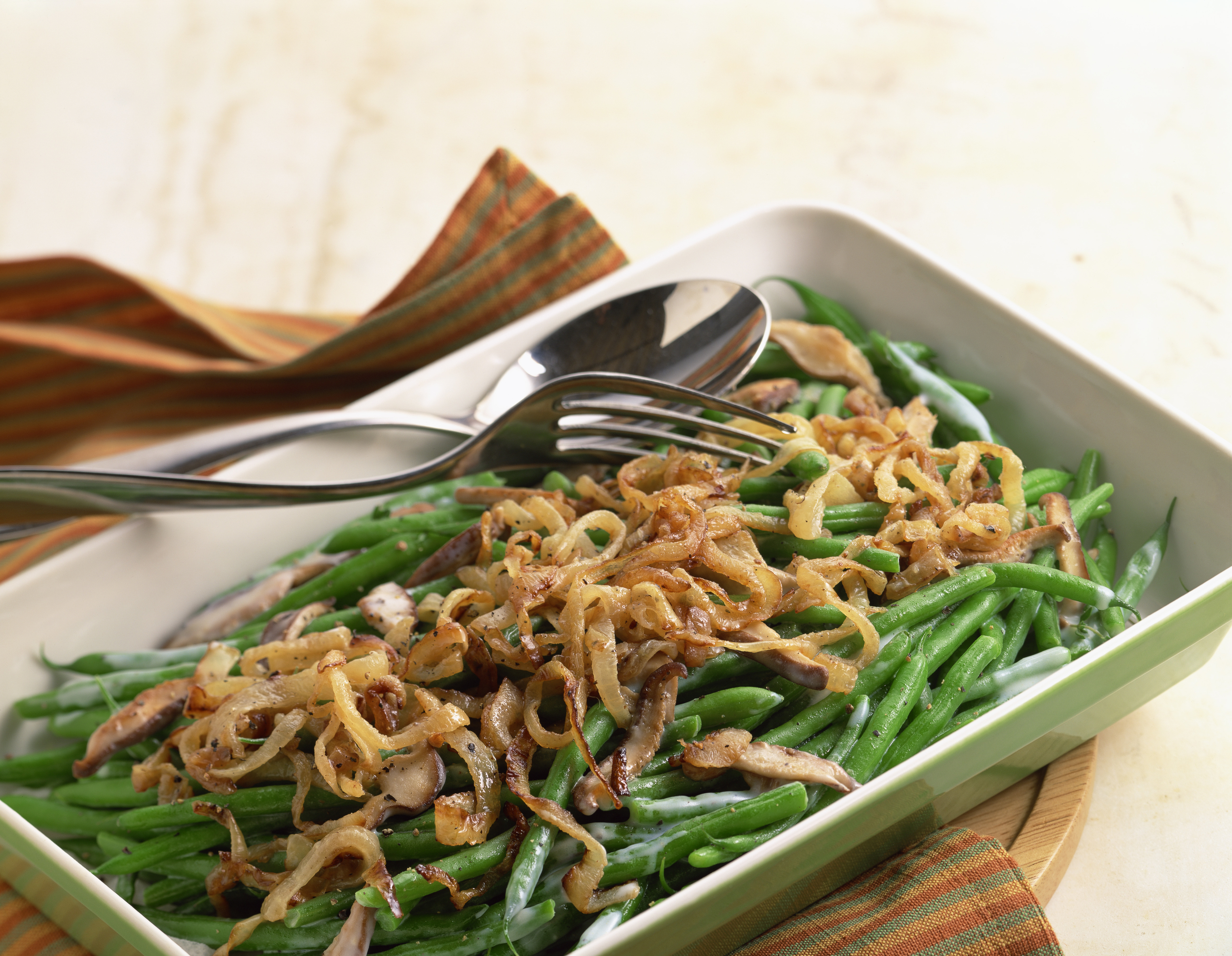 Green bean casserole topped with crispy onions, served in a rectangular dish with a fork and spoon on the side