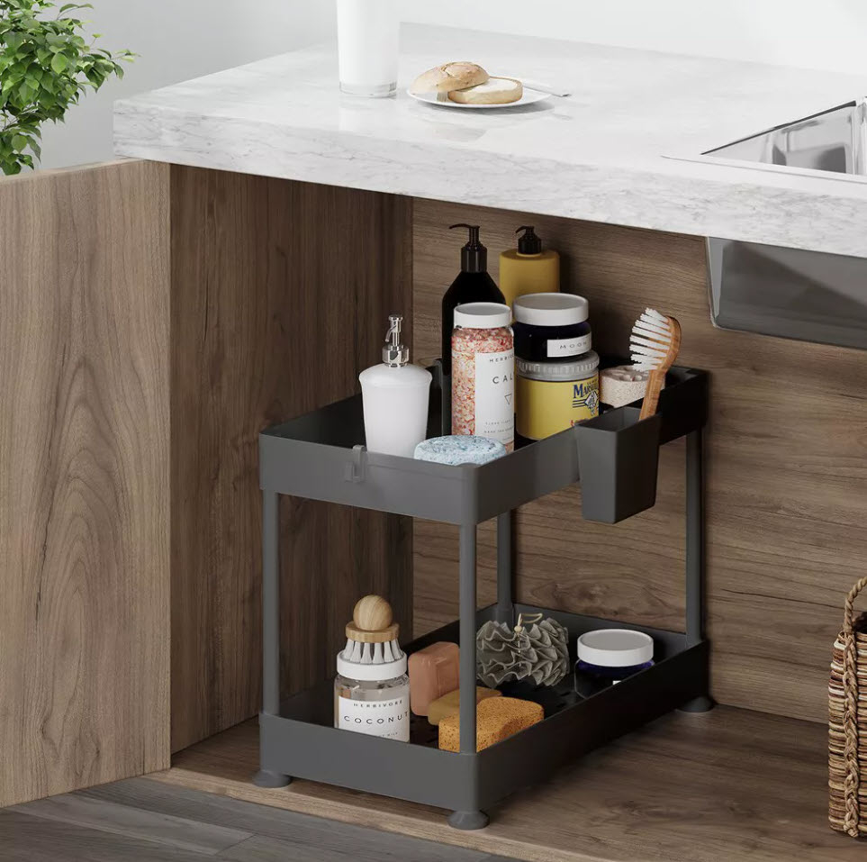 Under-sink organizer with various toiletries, soaps, and sponges neatly arranged on two shelves next to a kitchen counter