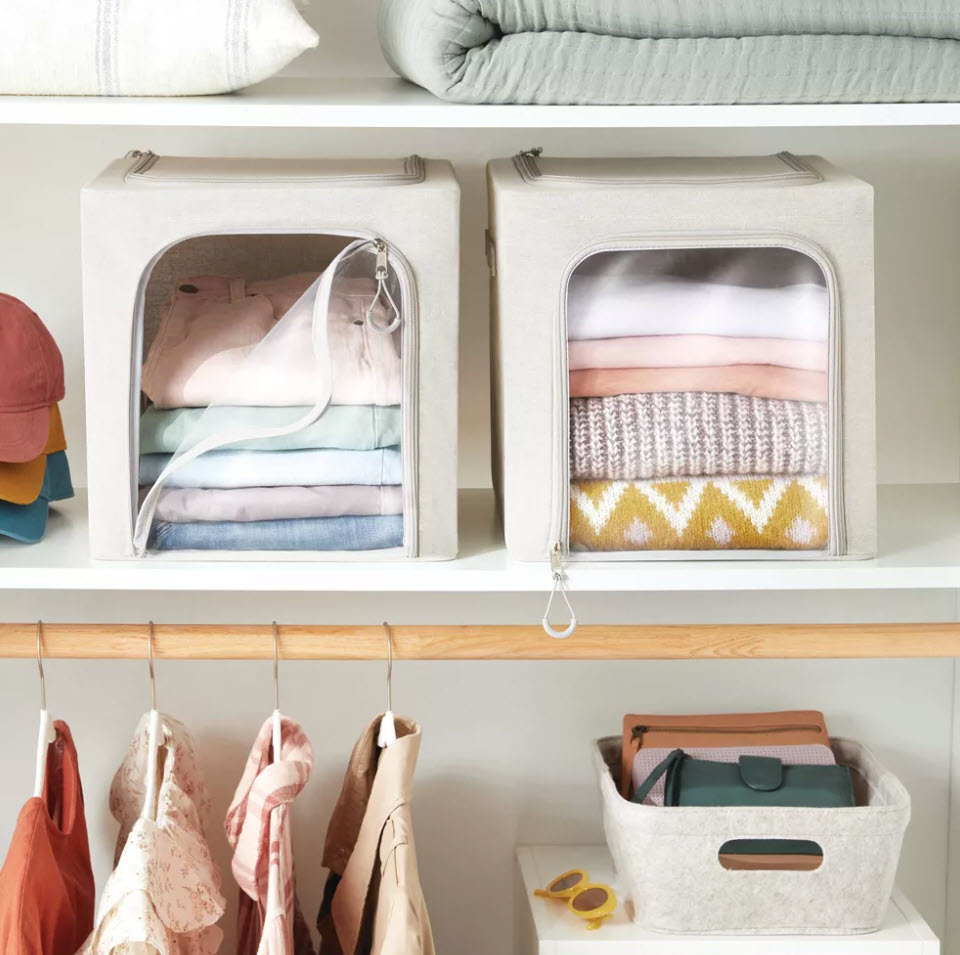 Folded clothes in beige storage boxes on a shelf, with clothes and hats hanging nearby