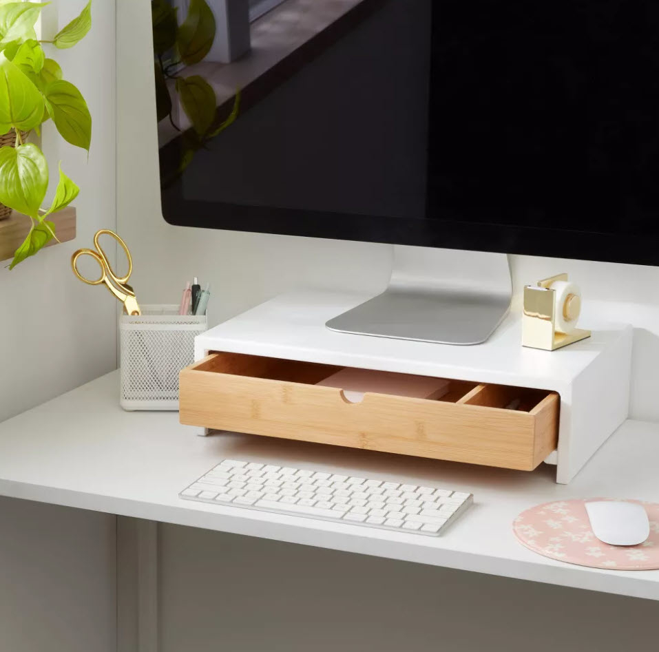 Modern desk setup with a monitor stand, keyboard, plants, and organized office supplies, creating a tidy and stylish workspace