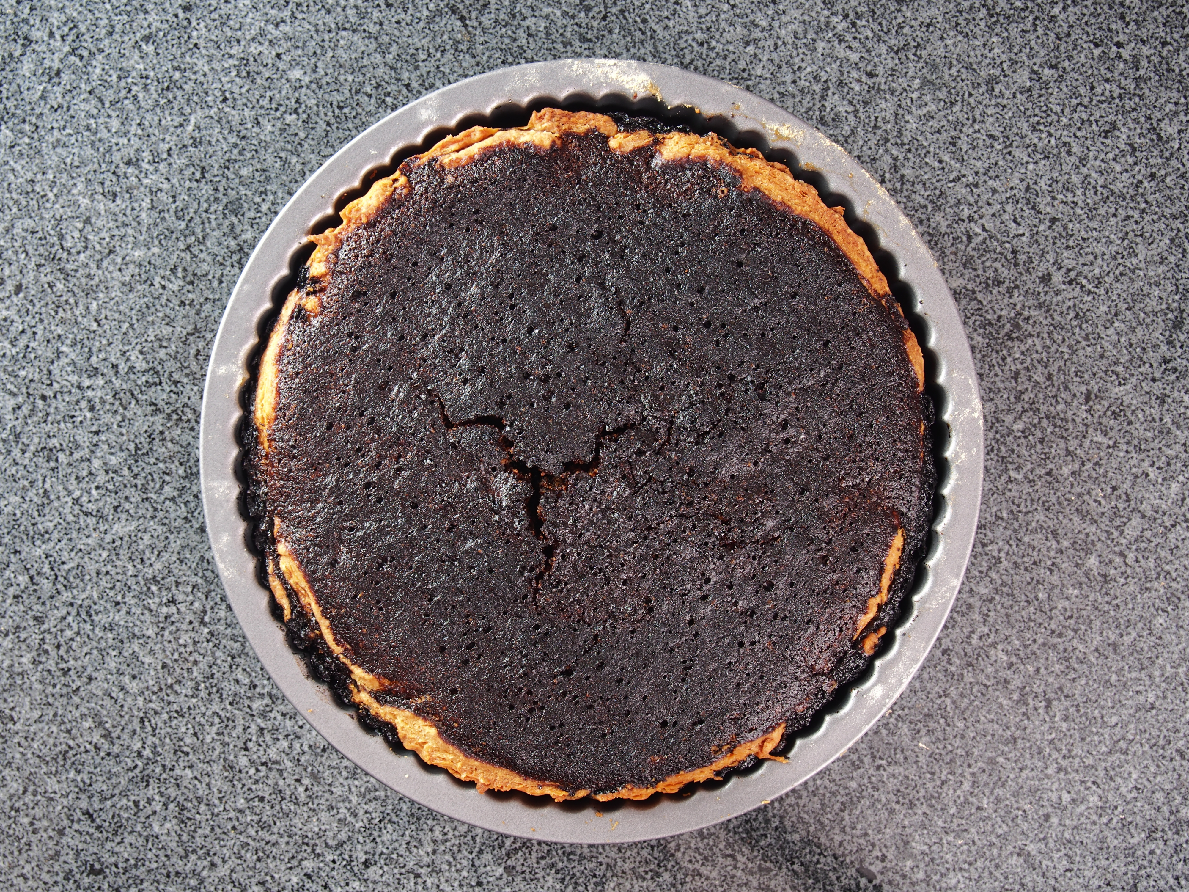 A burnt pie sits on a gray countertop, showing a dark, cracked surface