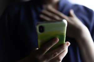 スマートフォンを手にした人物が画面を見つめ、胸に手を当てている。