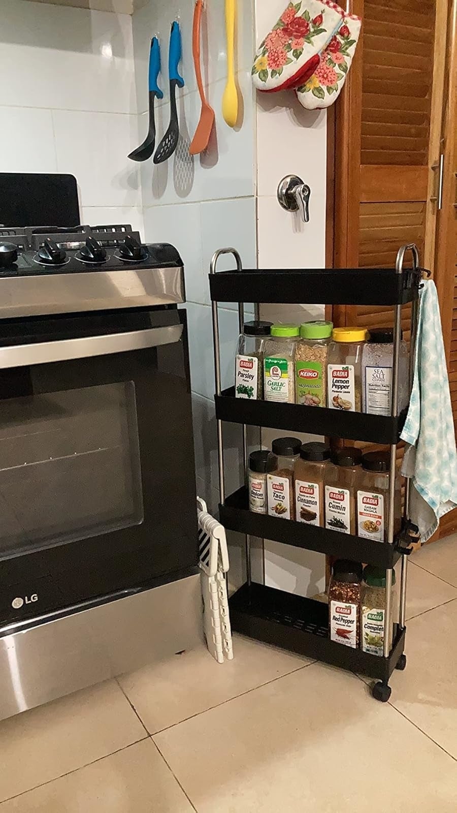 reviewer's kitchen cart on wheels fits between stove and wall and is filled spice rack filled with various labeled spice jars
