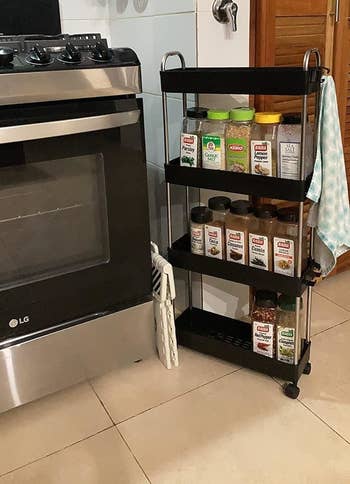 reviewer's kitchen cart on wheels fits between stove and wall and is filled spice rack filled with various labeled spice jars